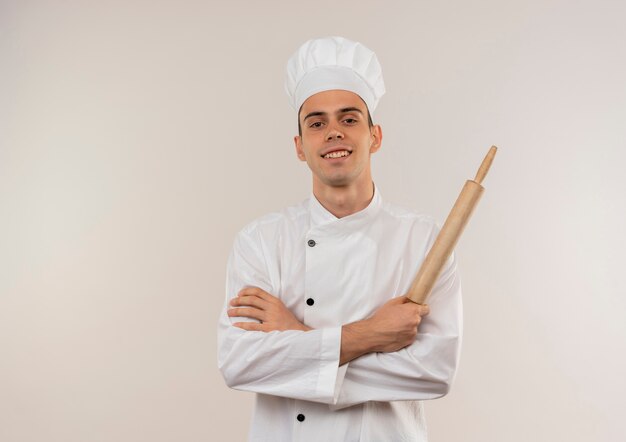 Lächelnder junger männlicher Koch, der Kochuniform trägt, die Hände hält, die Nudelholz mit Kopienraum halten