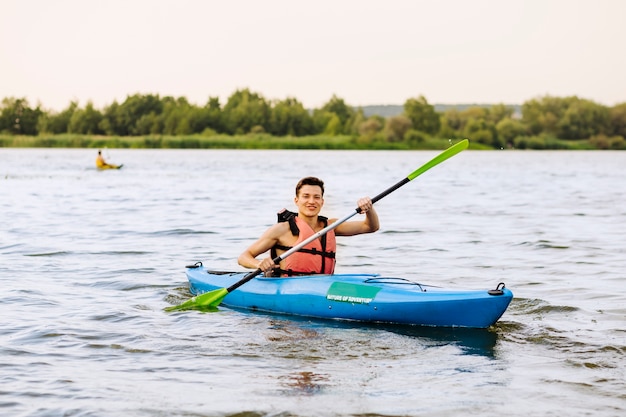 Lächelnder junger Mann, der auf See Kayak fährt