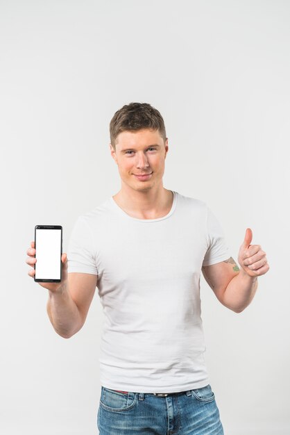 Lächelnder junger Mann, der Daumen herauf das Zeichen zeigt intelligentes Telefon gegen weißen Hintergrund zeigt
