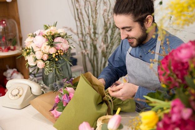 Lächelnder junger Mann, der den Blumenblumenstrauß im Blumenladen einwickelt