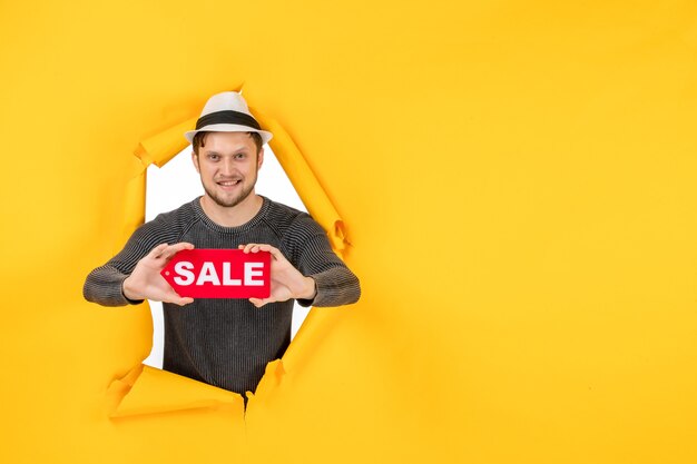 Lächelnder junger Mann, der ein Verkaufsschild in einer zerrissenen gelben Wand hält und zeigt