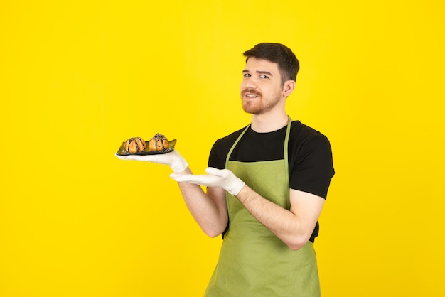 Lächelnder junger Mann, der frische hausgemachte Muffins hält und mit der Hand auf ein Gelb zeigt.