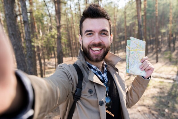 Lächelnder junger Mann, der in der Hand die Karte nimmt selfie im Wald hält