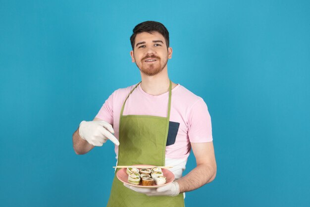 Lächelnder junger Mann, der Kuchenscheiben hält und mit dem Finger darauf zeigt.