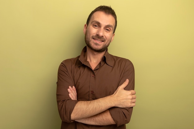 Lächelnder junger Mann, der mit geschlossener Haltung steht und Front lokalisiert auf olivgrüner Wand betrachtet