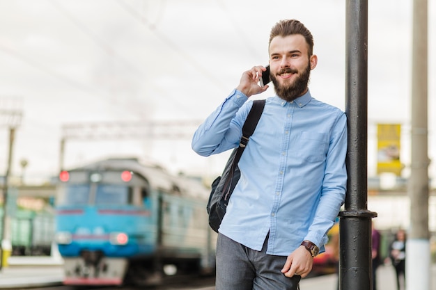 Lächelnder junger Mann, der Mobiltelefon am Bahnhof verwendet