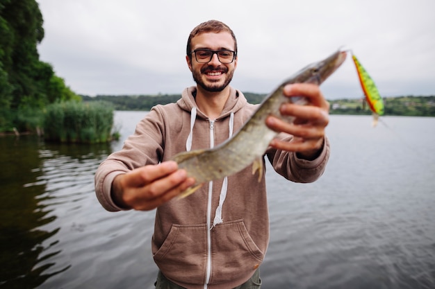 Kostenloses Foto lächelnder junger mann, der süßwasserfische mit köder hält