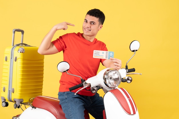Lächelnder junger Mann der Vorderansicht auf Moped, der Ticket auf gelbem Hintergrund hält