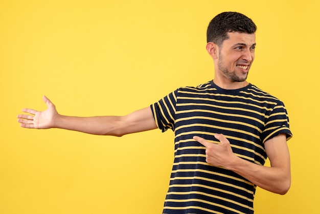 Lächelnder junger Mann der Vorderansicht im gelben isolierten Hintergrund des gestreiften Schwarzweiss-T-Shirts