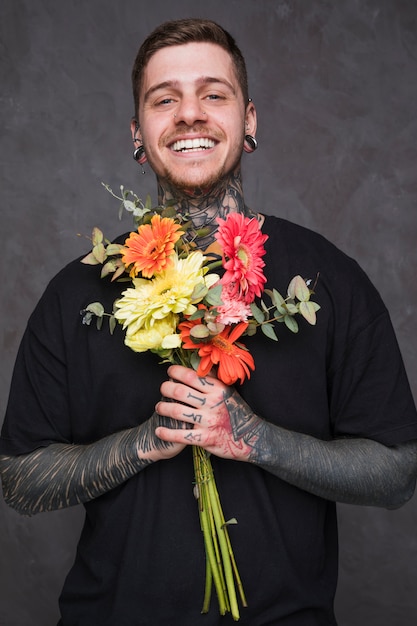 Lächelnder junger Mann mit den durchbohrten Ohren und Nase, die in der Hand Blumenstrauß betrachtet Kamera hält