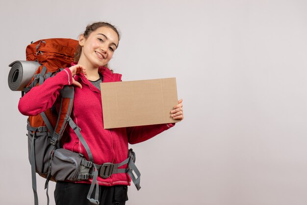 Kostenloses Foto lächelnder junger reisender mit großem rucksack, der pappe auf grau hält