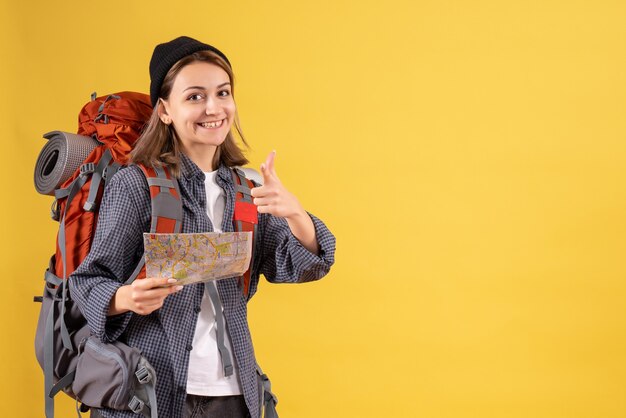 lächelnder junger Reisender mit Rucksack, der eine auf die Kamera gerichtete Karte hält