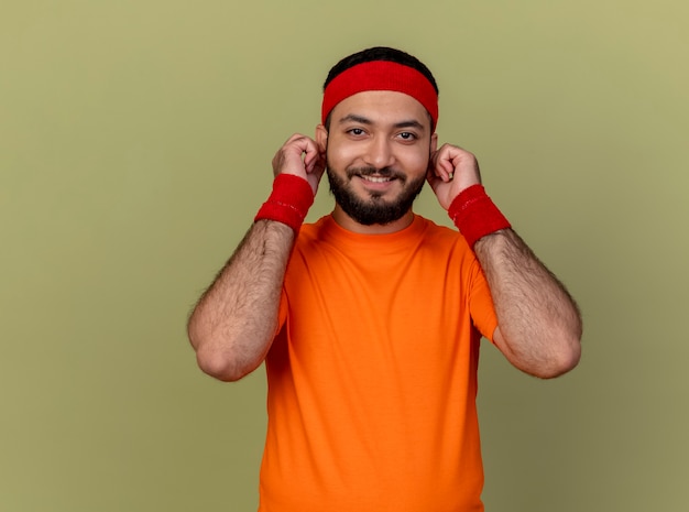 Lächelnder junger sportlicher Mann, der Stirnband und Armband hält, die Ohren lokalisiert auf olivgrün halten