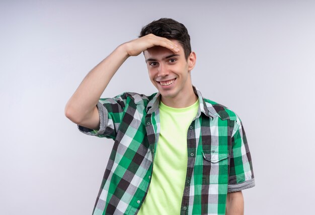 Lächelnder kaukasischer junger Mann, der grünes Hemd trägt Kamera mit Hand auf lokalisiertem weißem Hintergrund betrachtet