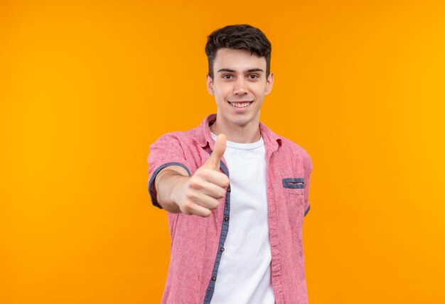 Lächelnder kaukasischer junger Mann, der rosa Hemd seinen Daumen oben auf lokalisiertem orange Hintergrund trägt