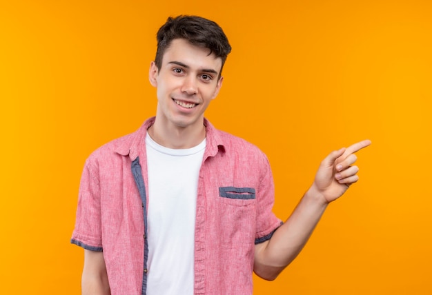 Lächelnder kaukasischer junger Mann, der rosa Hemd trägt, zeigt auf lokalisierten orange Hintergrund zur Seite