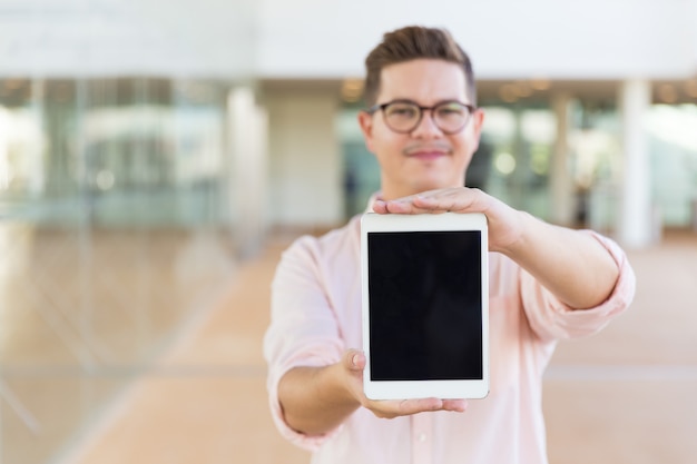 Lächelnder Kerl in den Gläsern, die leeren Tablettenschirm zeigen