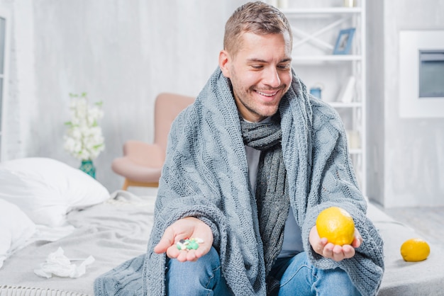 Kostenloses Foto lächelnder kranker mann, der auf dem bett in der hand wundernd für vollständige zitrone oder pillen sitzt