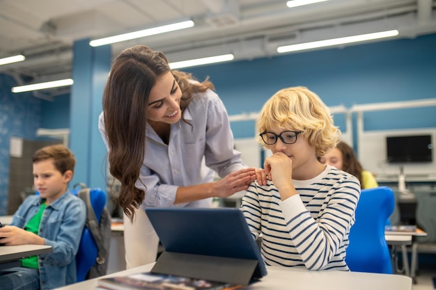 Lächelnder Lehrer, der die Schulter eines Jungen berührt, der auf Tablet schaut