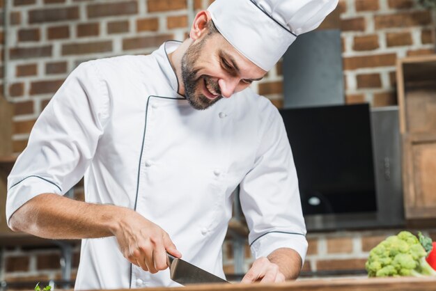 Lächelnder männlicher Chef, der Gemüse hackt