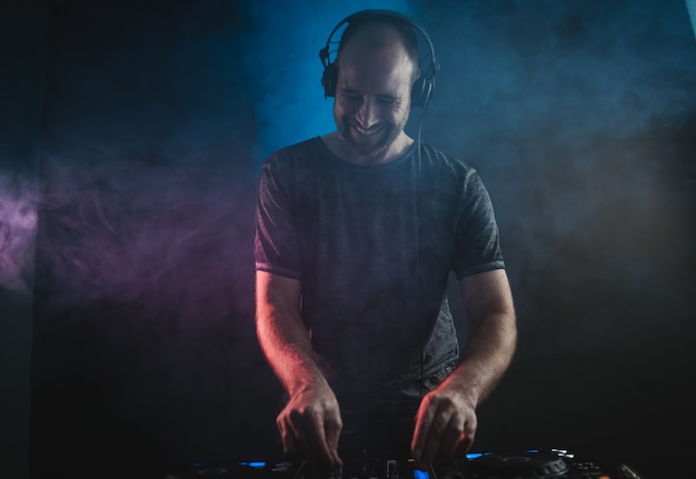 Lächelnder männlicher DJ, der unter den Lichtern gegen eine Dunkelheit arbeitet