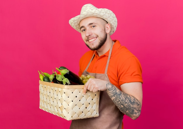 Lächelnder männlicher Gärtner mit Gartenhut hält Gemüsekorb
