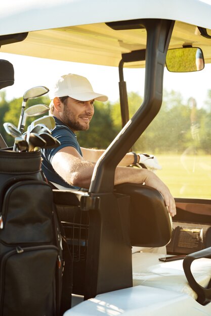 Lächelnder männlicher Golfer, der in einem Golfwagen sitzt