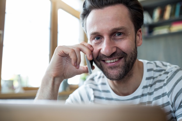 Lächelnder Mann auf dem Handy in der Kaffeestube im Gespräch