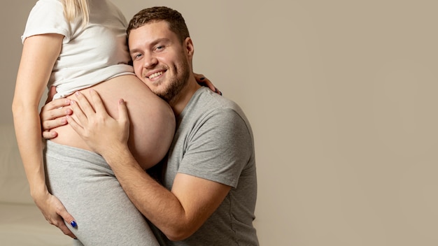 Lächelnder Mann, der auf den Bauch seiner schwangeren Frau hört