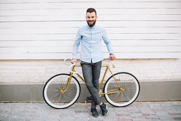 Kostenloses Foto lächelnder mann, der auf fahrrad nahe wand sich lehnt