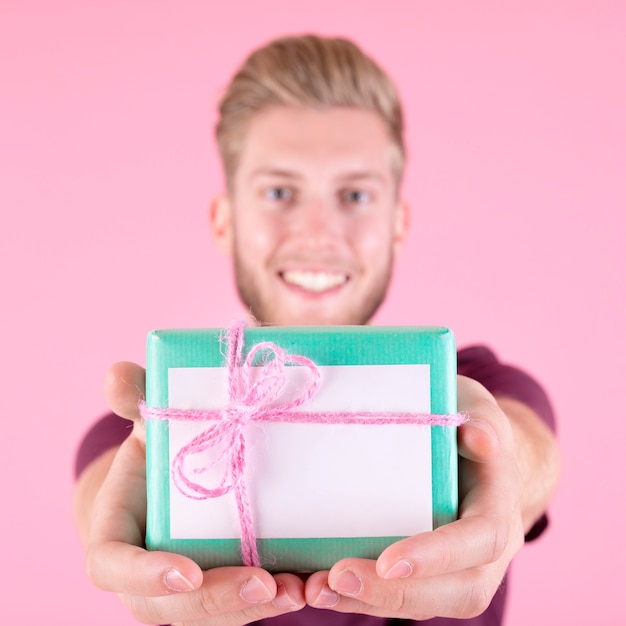 Lächelnder Mann, der die eingewickelte Geschenkbox gebunden mit rosa Schnur anbietet