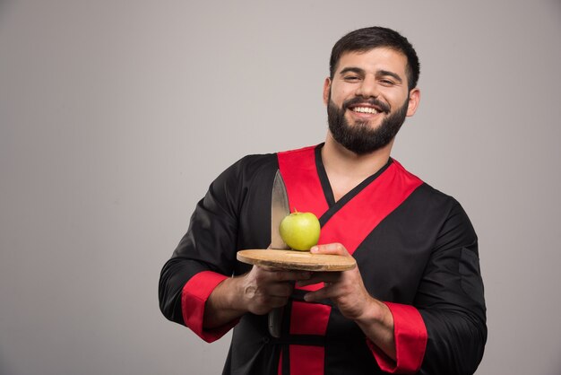 Lächelnder Mann, der einen Apfel mit Messer auf Holzbrett hält.