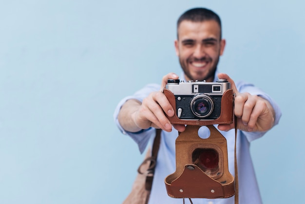 Lächelnder Mann, der Foto mit der Retro- Kamera steht gegen blaue Wand macht