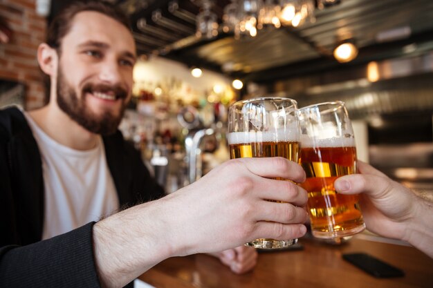 lächelnder Mann, der Gläser mit Freund in der Bar anstößt