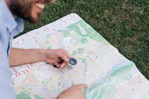 Kostenloses Foto lächelnder mann, der kompass hält und auf karte auf gras zeigt