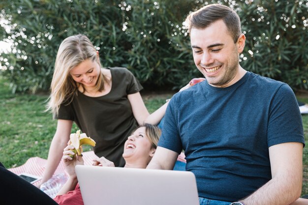 Lächelnder Mann, der Laptop auf Picknick mit Freunden verwendet