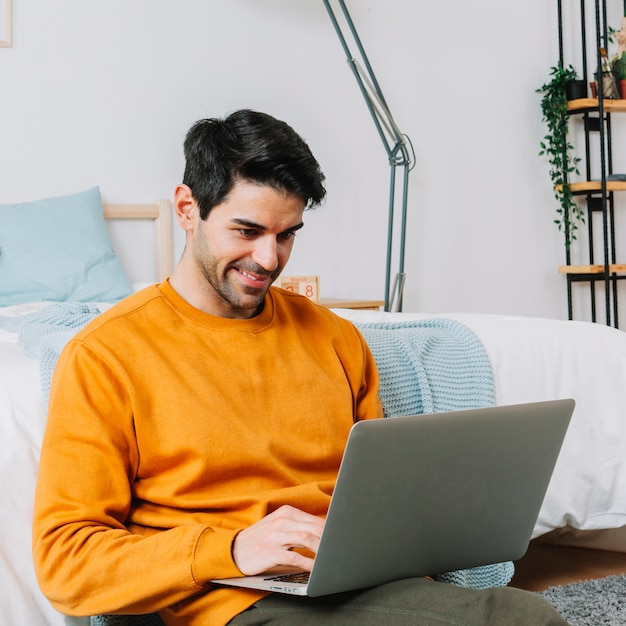 Kostenloses Foto lächelnder mann, der laptop nahe bett verwendet