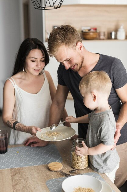 Lächelnder Mann, der Portionshafer des kleinen Jungen zu seiner Mutterhalteplatte betrachtet