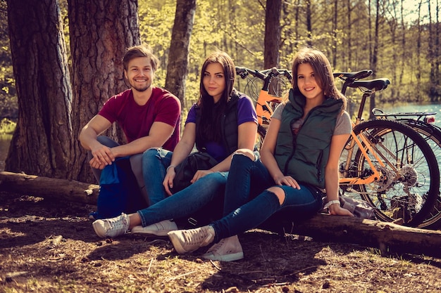 Lächelnder Mann mit zwei attraktiven Frauen, die sich nach einer Fahrradtour in einem Wald entspannen.