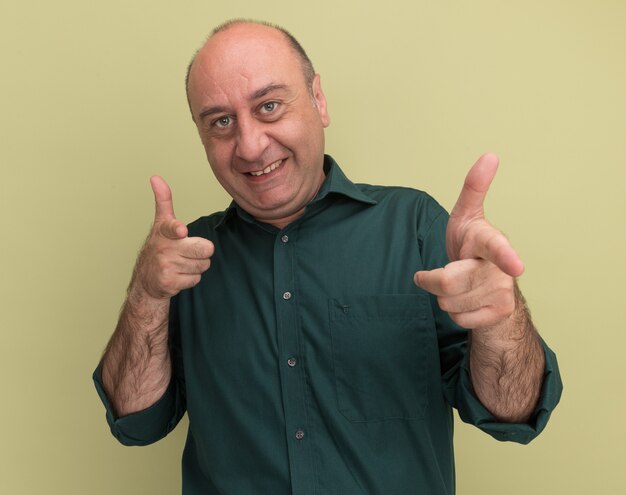 Lächelnder Mann mittleren Alters, der grüne T-Shirt-Punkte trägt, lokalisiert auf olivgrüner Wand