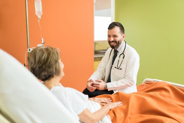 Lächelnder medizinischer Mitarbeiter in der Mitte des Erwachsenen, der mit einem älteren Patienten im Krankenhaus über Krankheiten spricht