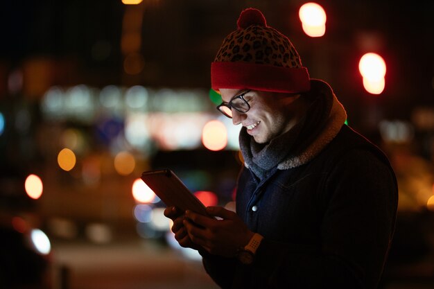 Lächelnder moderner Mann in den Brillen, die seinen Handy verwenden