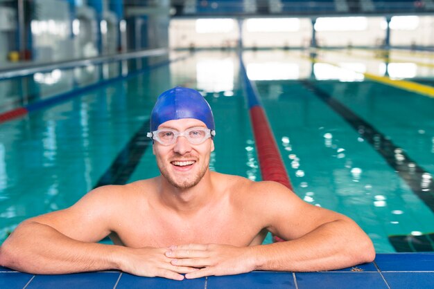 Lächelnder Schwimmer, der auf Rand des Pools stationiert