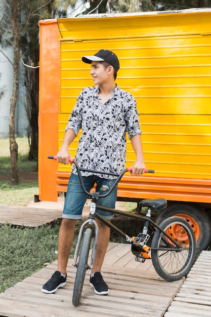 Lächelnder stilvoller teenager mit seinem fahrrad, das weg schaut