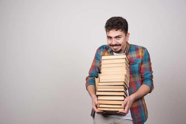 Lächelnder Student mit Stapel Büchern, die Kamera betrachten.