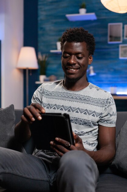 Lächelnder Typ mit Tablet-Computer, der im Internet surft und in den sozialen Medien nach Freizeit zu Hause im Wohnzimmer sucht. Freiberufler, der nach Informationen für Online-Lektionen sucht. Heimarbeit
