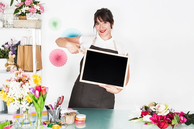 Lächelnder weiblicher Florist, der auf unbelegten Schiefer im Blumenshop zeigt