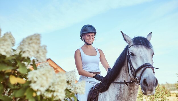 Lächelnder weiblicher Jockey auf einem Apfelschimmel, der durch den blühenden Garten geht.