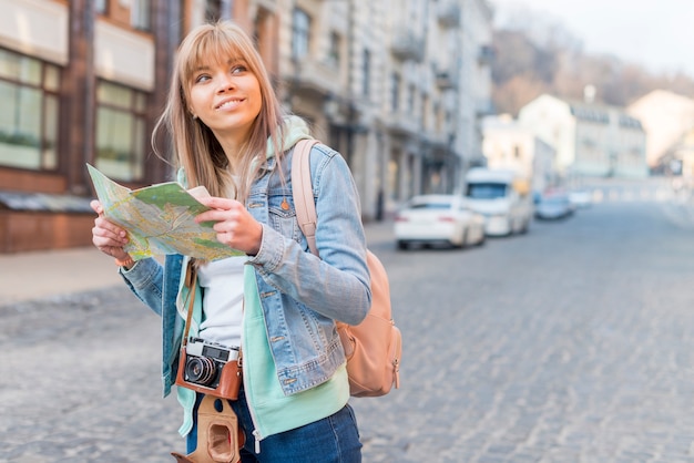 Lächelnder weiblicher Reisender, der auf Hintergrund der städtischen Landschaft mit Karte steht