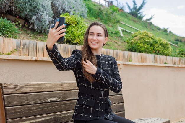 Lächelndes Blogger-Mädchen macht Selfie mit ihrem Smartphone, indem sie Haare im Park hält